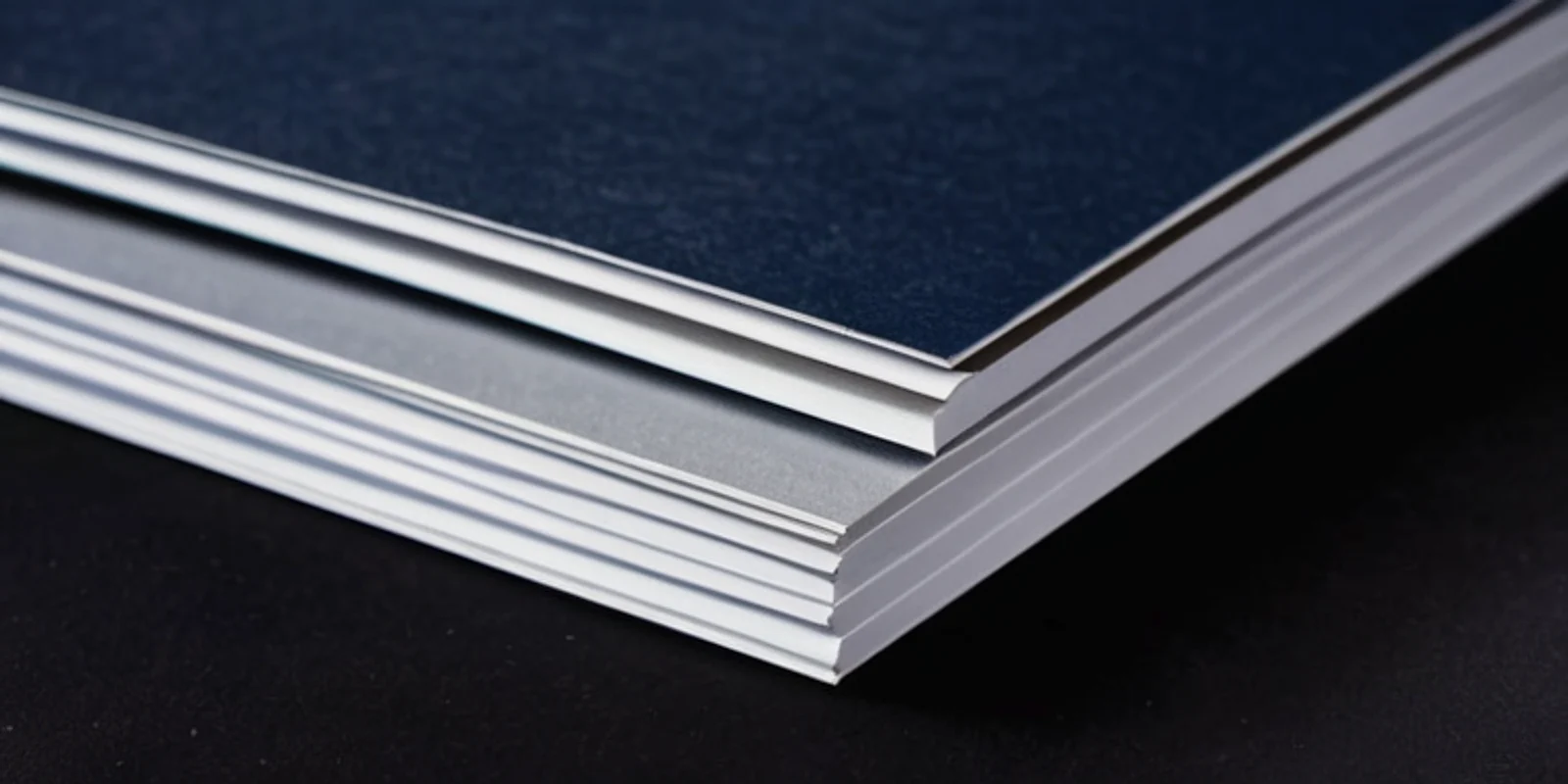 A neat stack of blank white sheets under a dark navy cover on a dark desk.