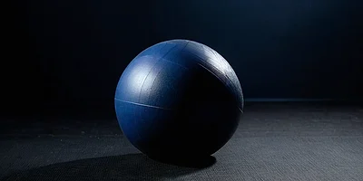 A smooth navy exercise ball on a dark rubber gym floor under a single overhead light.